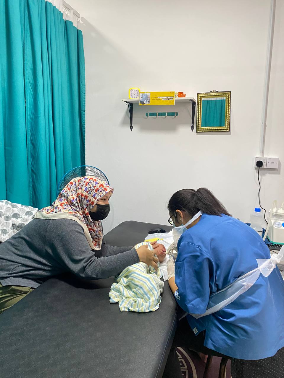 Fisioterapis sedang lakukan proses sedut kahak bayi yang alami batuk dan selsema sambil diperhatikan oleh ibu bayi tersebut